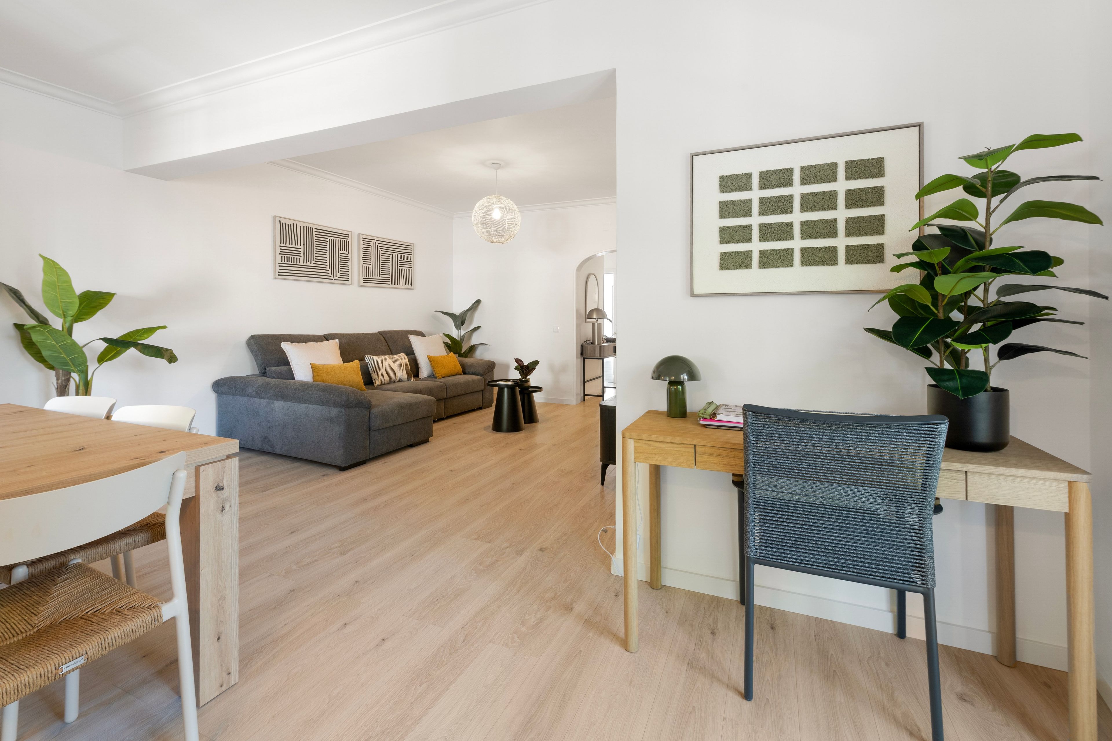 A modern living room with a grey sofa, wooden coffee table, and a dining area with a wooden table and chairs.