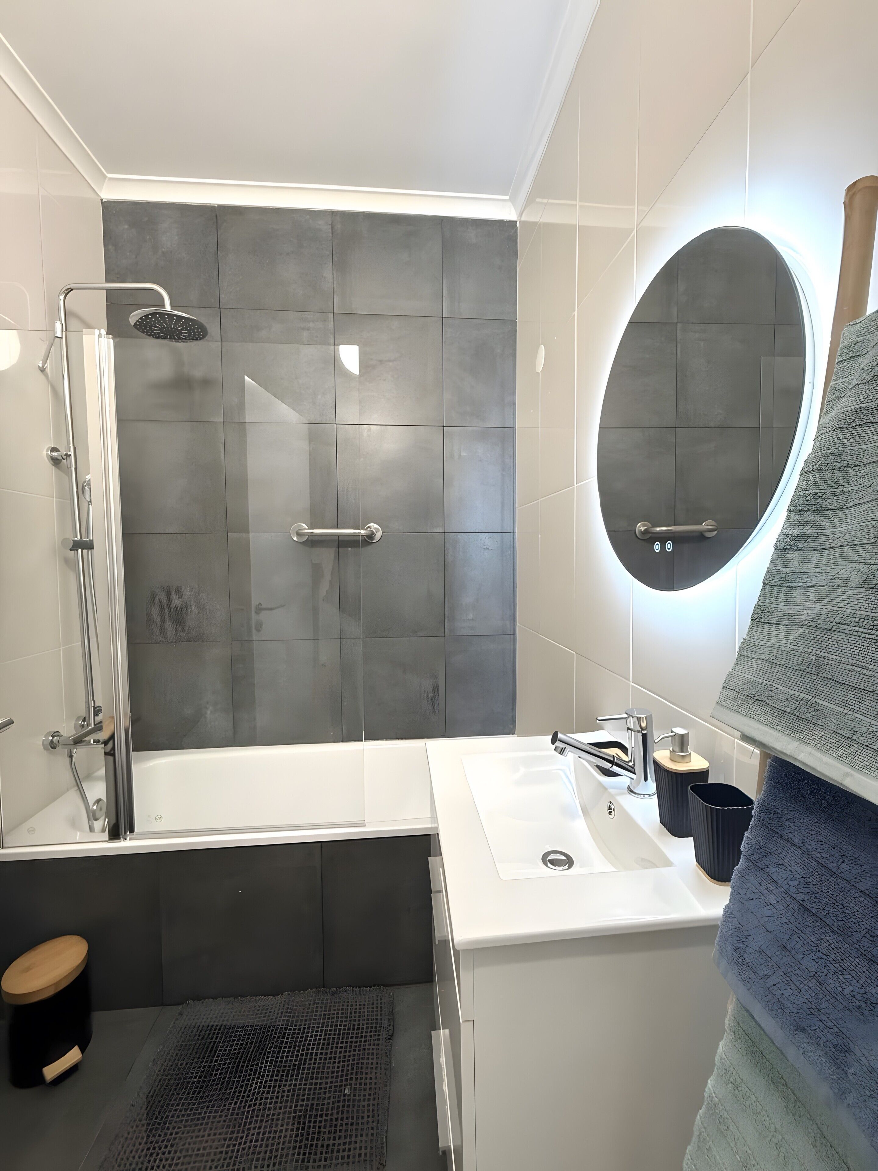 Een moderne badkamer met een douchecabine van glas, een ronde spiegel en een wit wastafelmeubel.