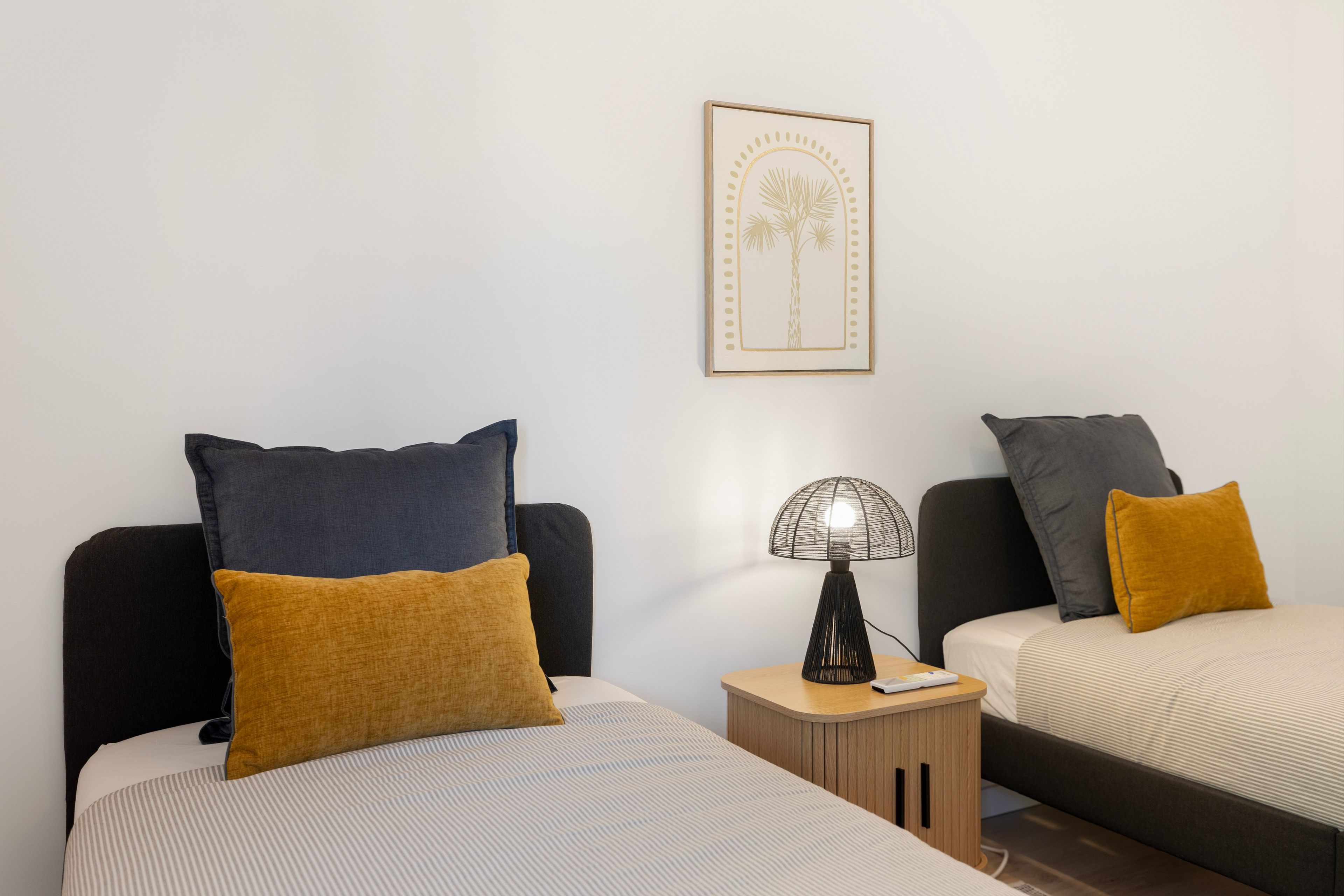 Une chambre d’hôtel avec deux lits, chacun agrémenté d’un oreiller de couleur différente, une table de chevet avec une lampe et un tableau encadré au mur.