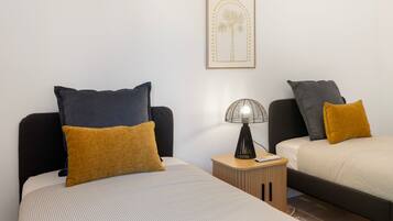 Une chambre d’hôtel avec deux lits, chacun agrémenté d’un oreiller de couleur différente, une table de chevet avec une lampe et un tableau encadré au mur.