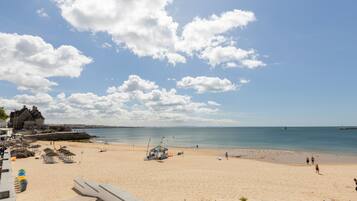 Ein Strand mit blauem Himmel, sandigem Ufer und einem Gebäude im Hintergrund.