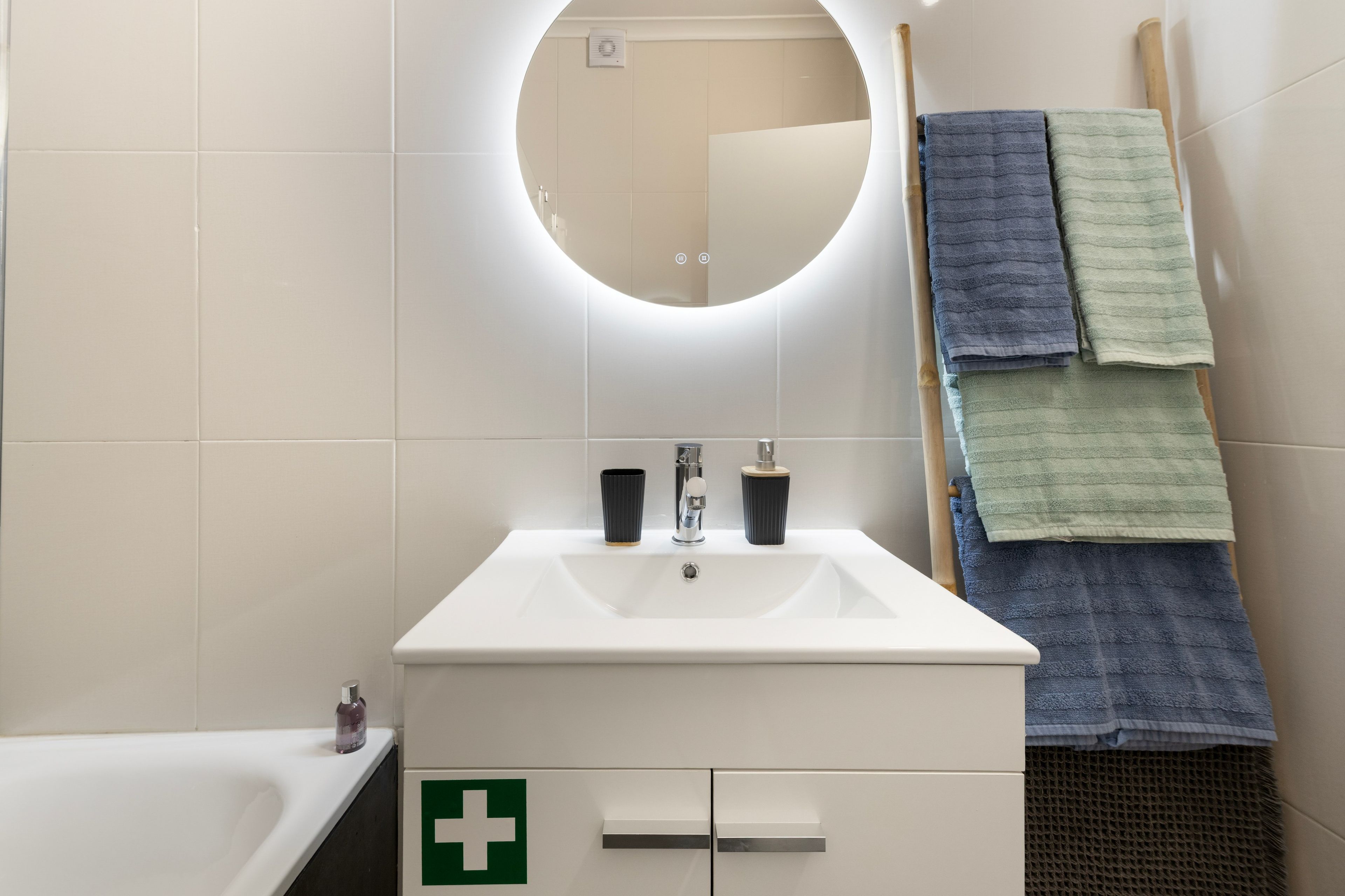 Een badkamer met een witte wasbak, een spiegel en een handdoekrek met meerdere handdoeken.