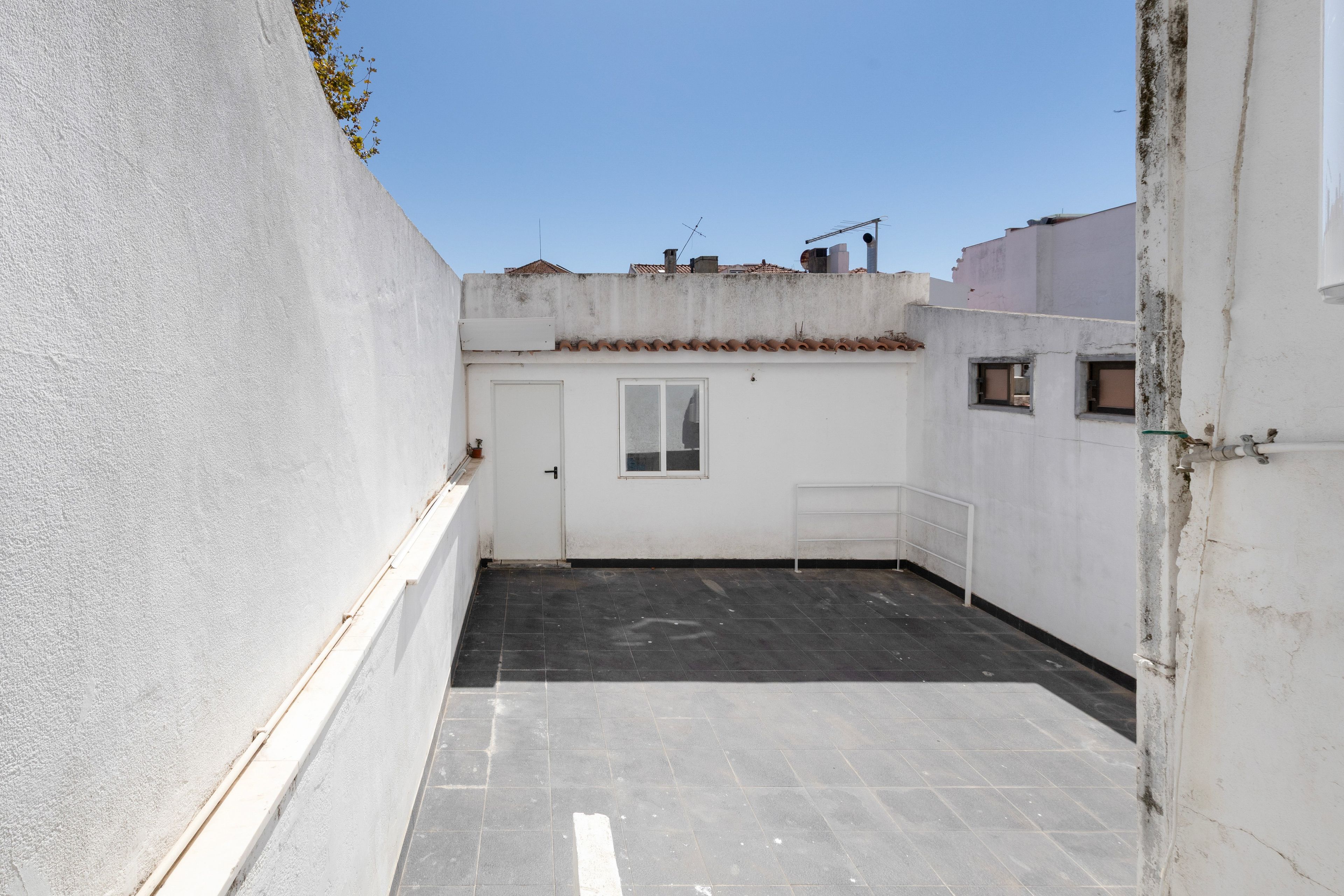 A narrow alleyway with a white door and a window, leading to a tiled patio area.