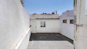 A narrow alleyway with a white door and a window, leading to a tiled patio area.