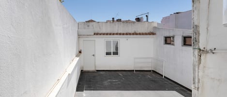 A narrow alleyway with a white door and a window, leading to a tiled patio area.