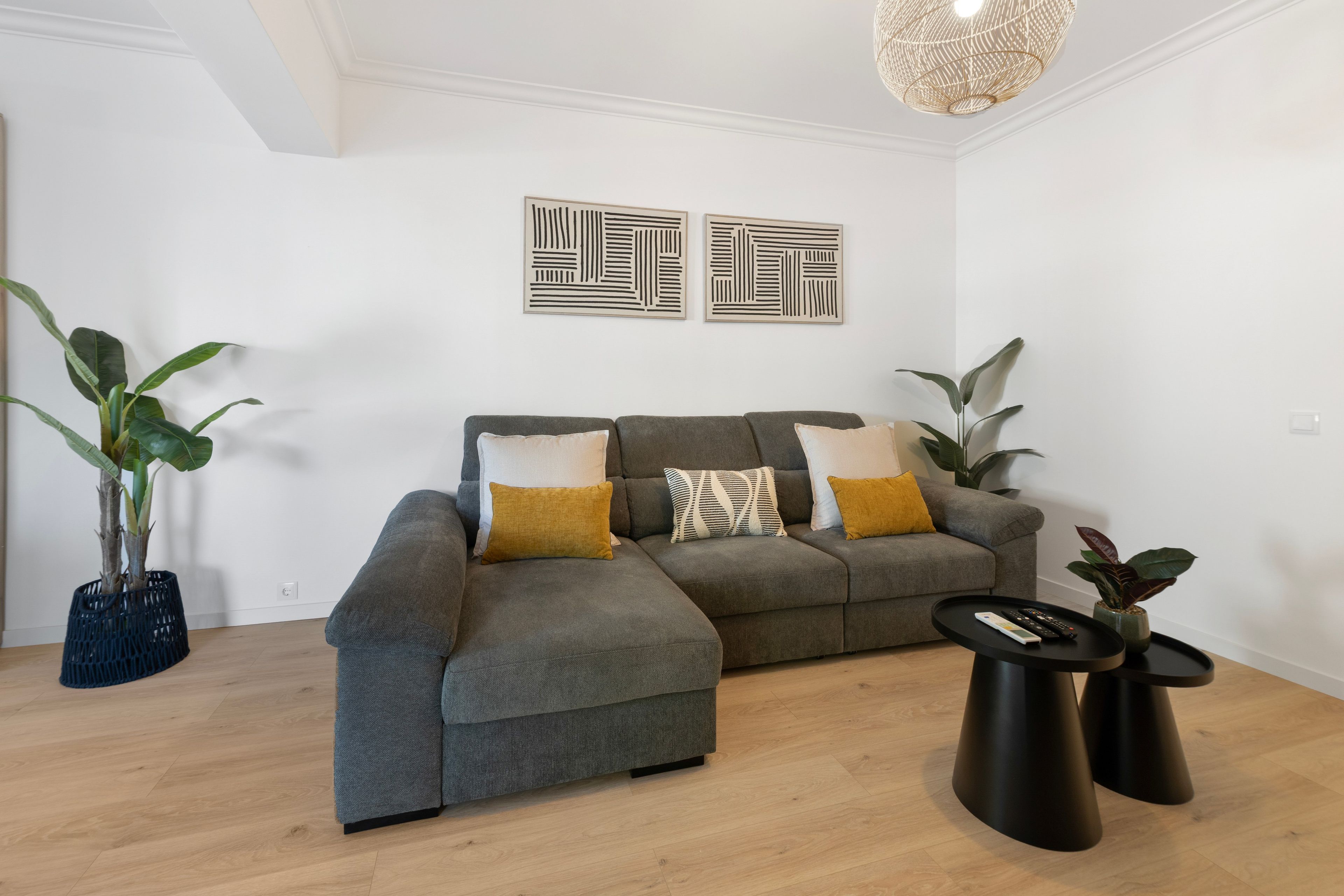 A modern living room with a grey sectional sofa, two black side tables, and a hanging light fixture.
