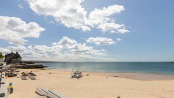 Une plage avec un ciel dégagé, un rivage sablonneux et un bâtiment en arrière-plan.