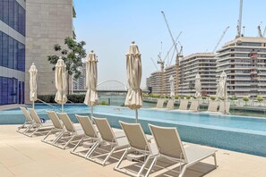 A poolside area with lounge chairs and umbrellas, a view of a construction site, and a modern building in the background. - Silkhaus Elite 2bdr With Canal View in Al Wasl (Dubai)