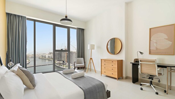 Una habitación de hotel moderna con una cama grande, un escritorio, una silla, un aparador y vistas a la ciudad.