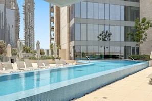A modern building with a swimming pool, lounge chairs, and umbrellas. - Silkhaus Elite 2bdr With Canal View in Al Wasl (Dubai)