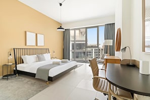 A hotel room with a bed, a desk, a chair, a large window with a view, and a ceiling light. - Silkhaus Elite 2bdr With Canal View in Al Wasl (Dubai)