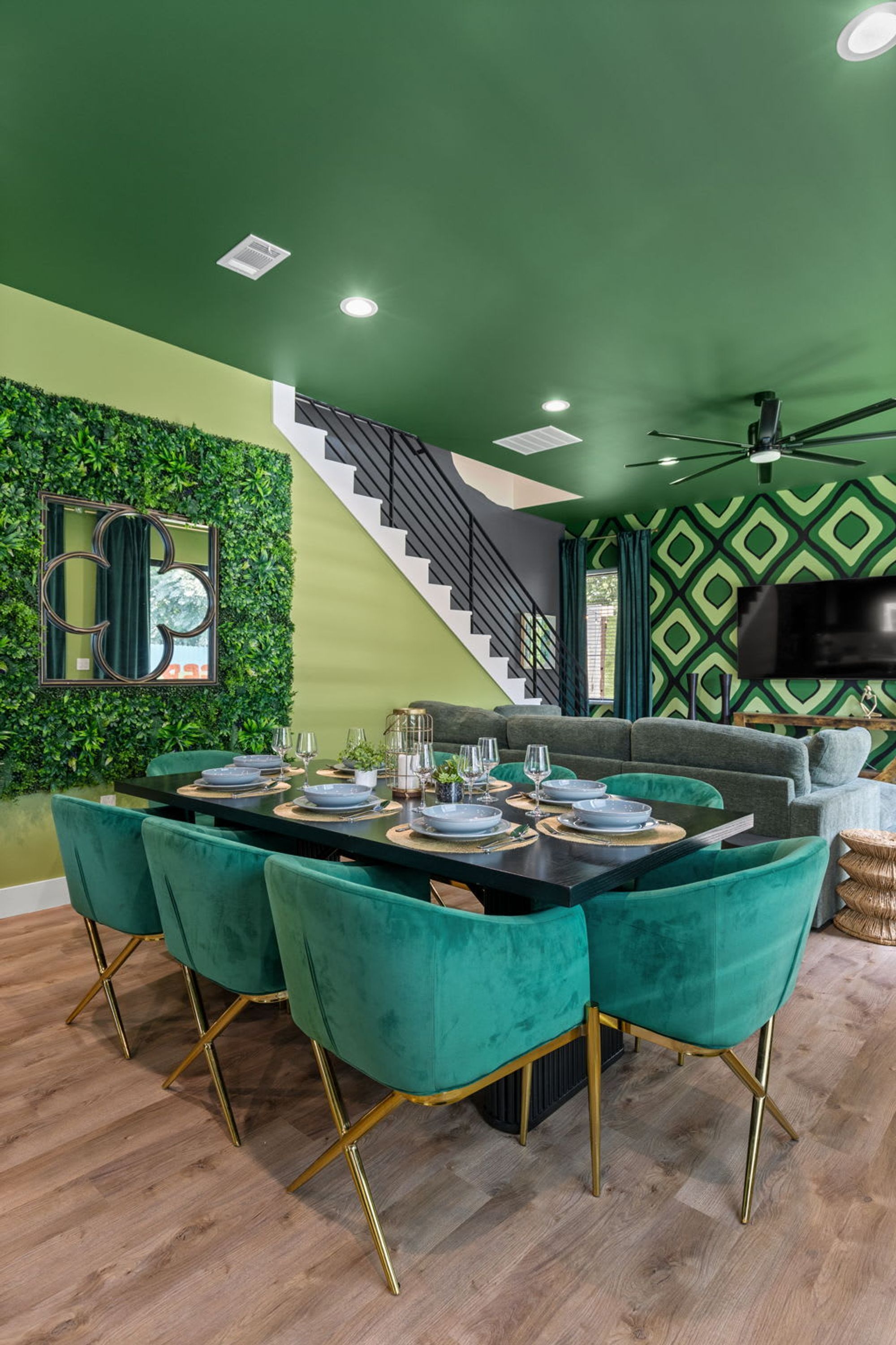 A dining area with a black table, teal chairs, and a staircase leading to a green-walled upper level.