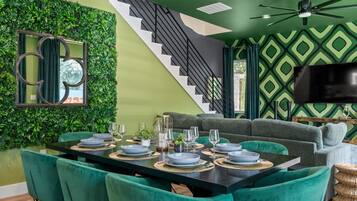 A dining area with a black table, teal chairs, and a staircase leading to a green-walled upper level.