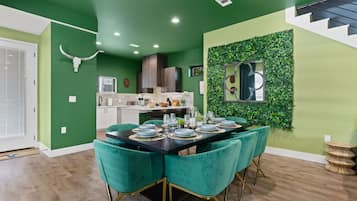 A dining area with a black table set for six, teal chairs, and a green accent wall with a mirror.