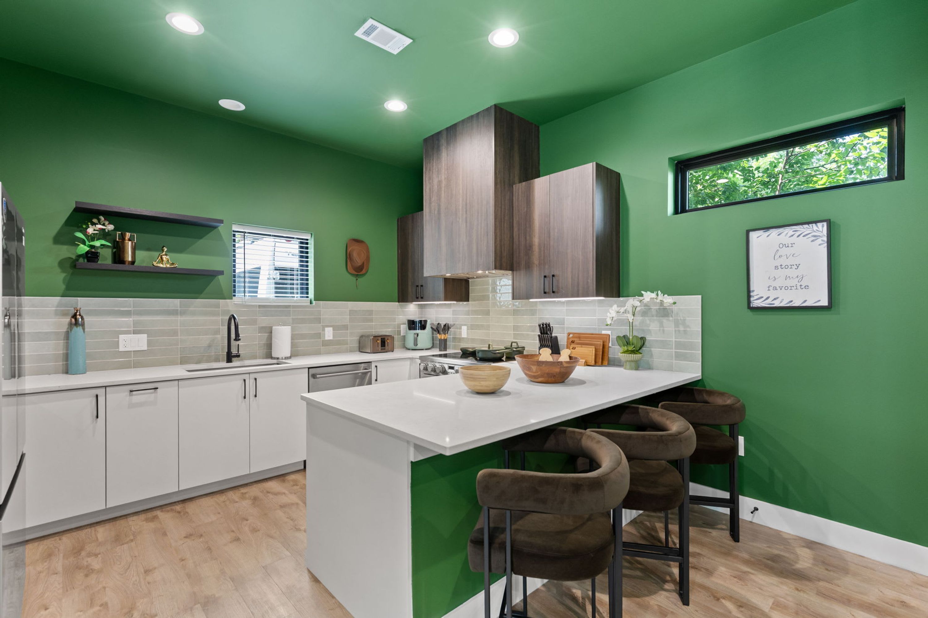 A modern kitchen with green walls, white cabinetry, and a central island with stools.