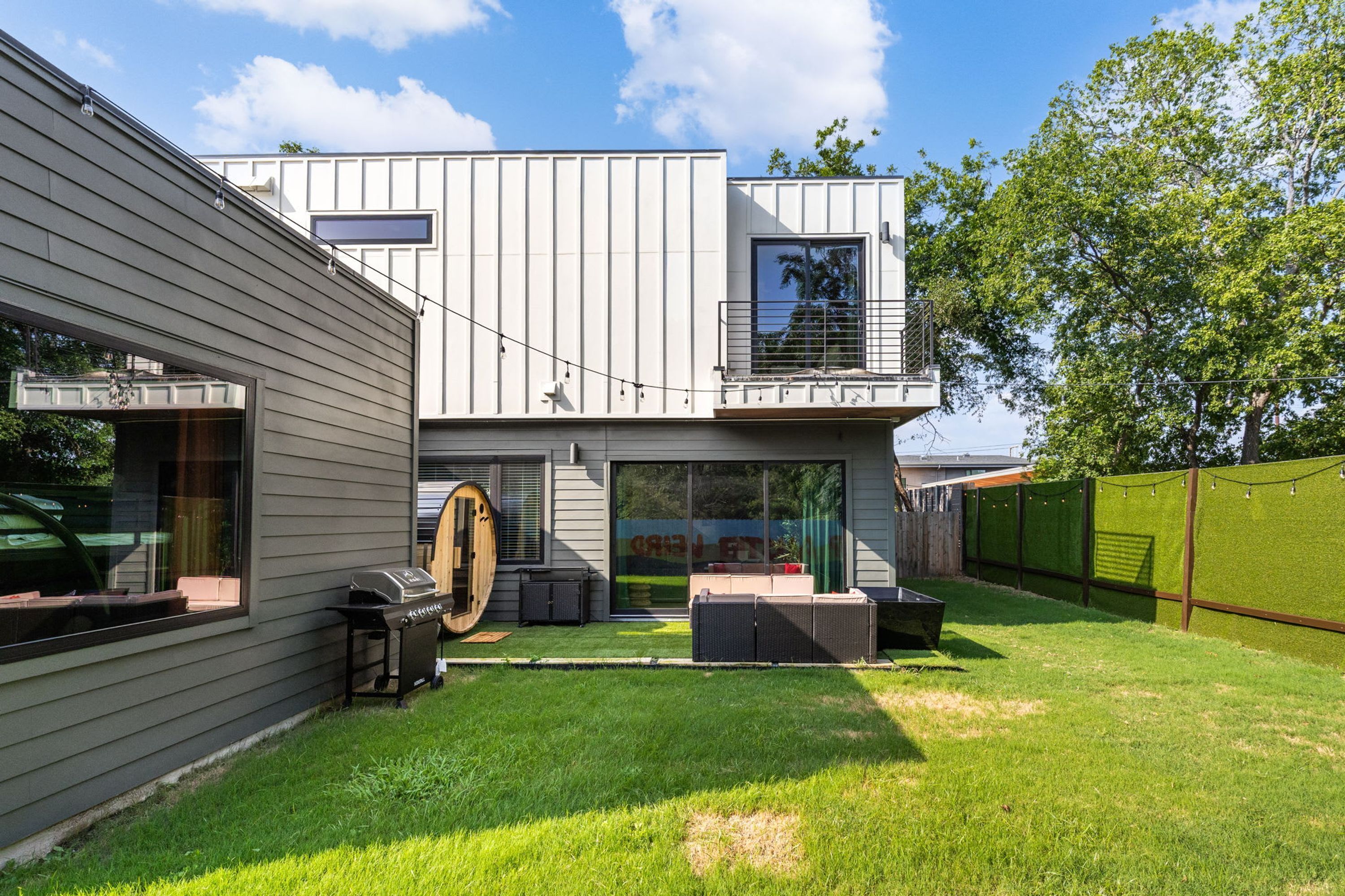 A modern two-story house with a covered patio, a barbecue grill, and a large sliding glass door.
