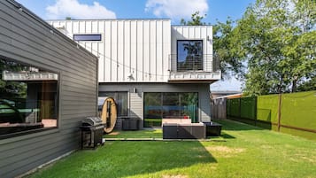 A modern two-story house with a covered patio, a barbecue grill, and a large sliding glass door.