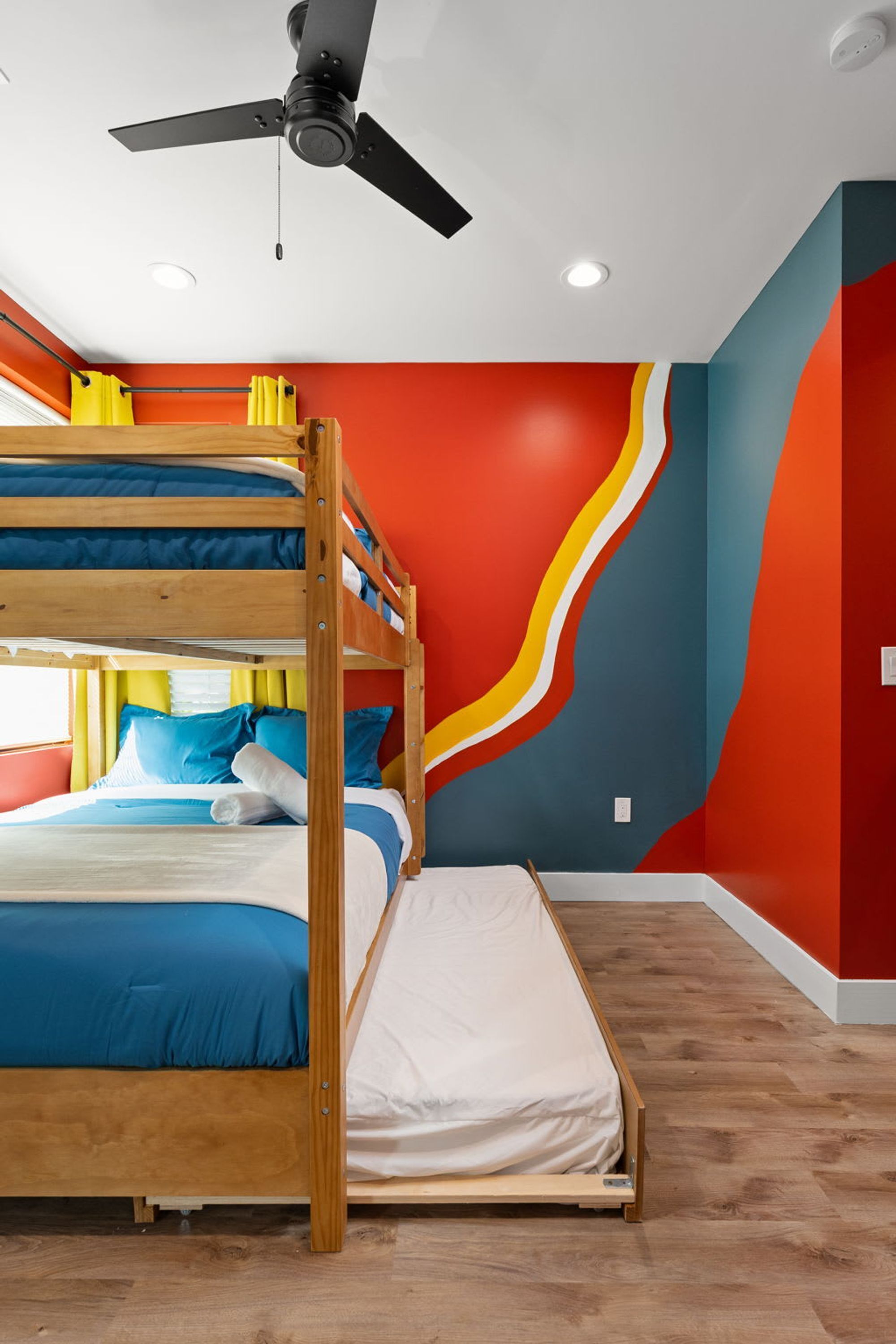 A bunk bed with a ceiling fan, a single bed, and a colorful wall design.