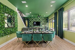 A dining area with a green-themed interior, including a wall with a geometric pattern, a ceiling fan, and a dining table set for six. - ATX 4BD Oasis w Sauna Cold Plunge Beauty Bar (Austin)