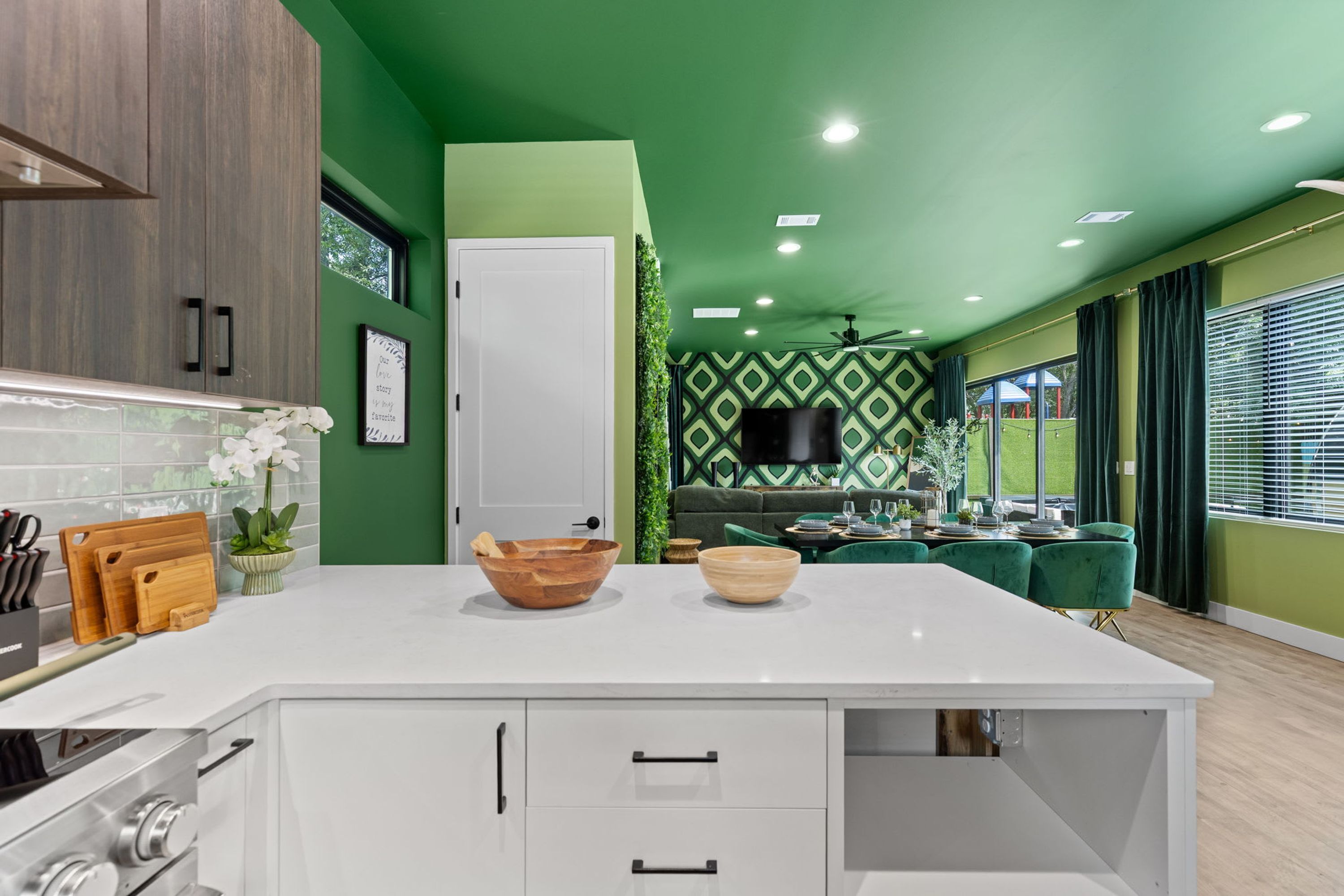 A modern kitchen with a white island, wooden cabinets, and a green accent wall.