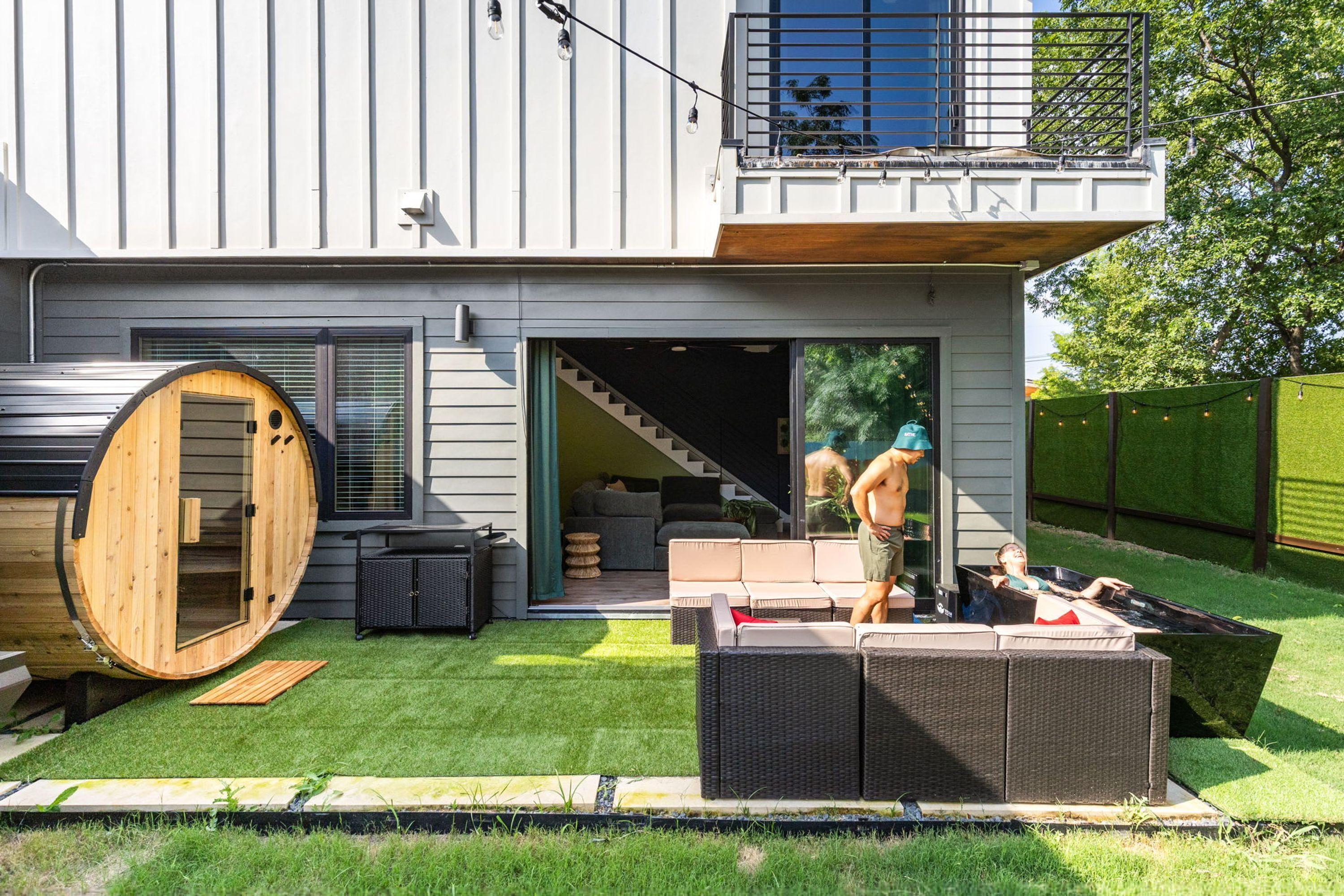 Une maison moderne dotée d’une grande cuve en bois, d’un espace salon extérieur et d’un escalier menant à un balcon.