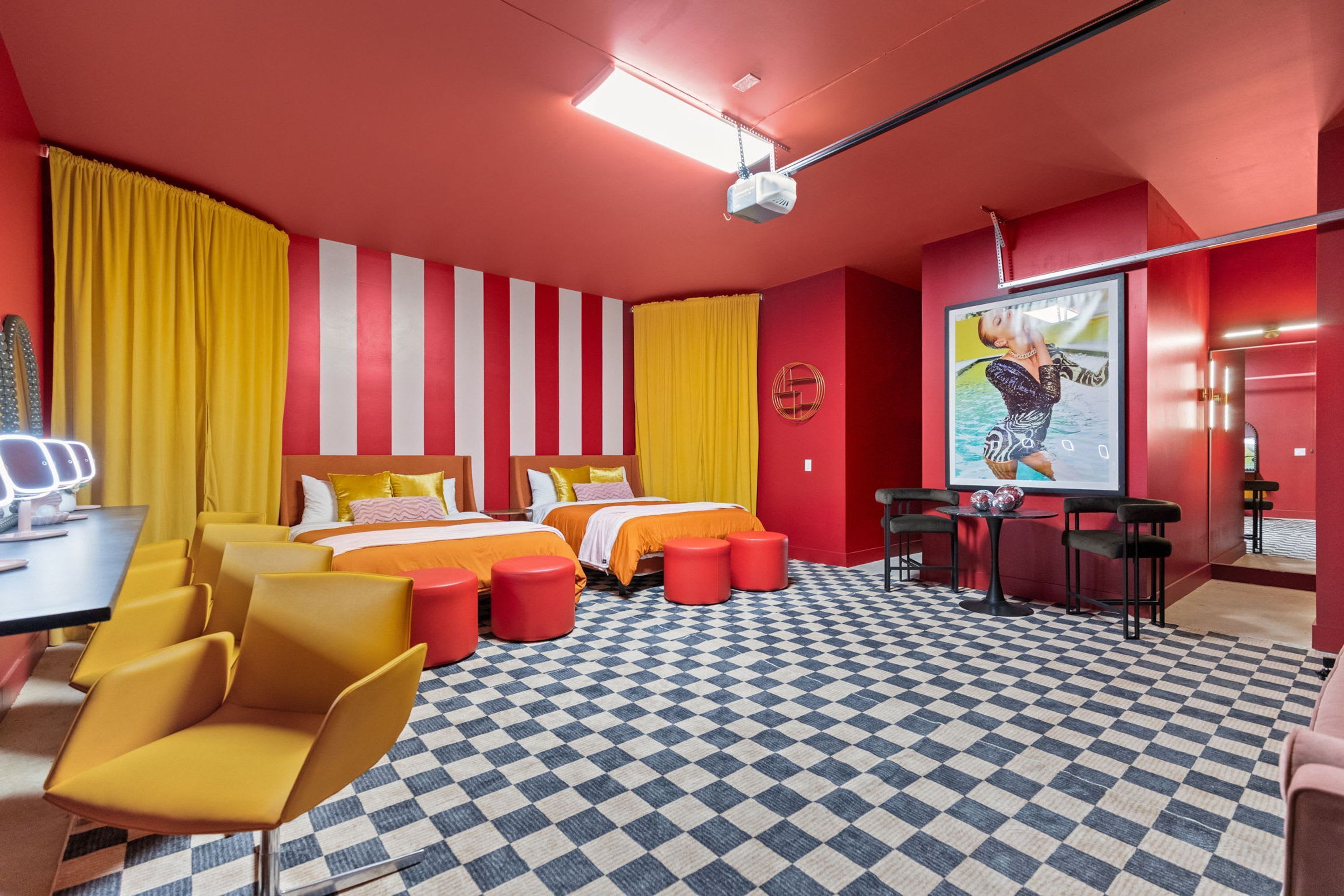 A hotel room with two beds, a desk, a chair, a table with two stools, and a checkered floor.