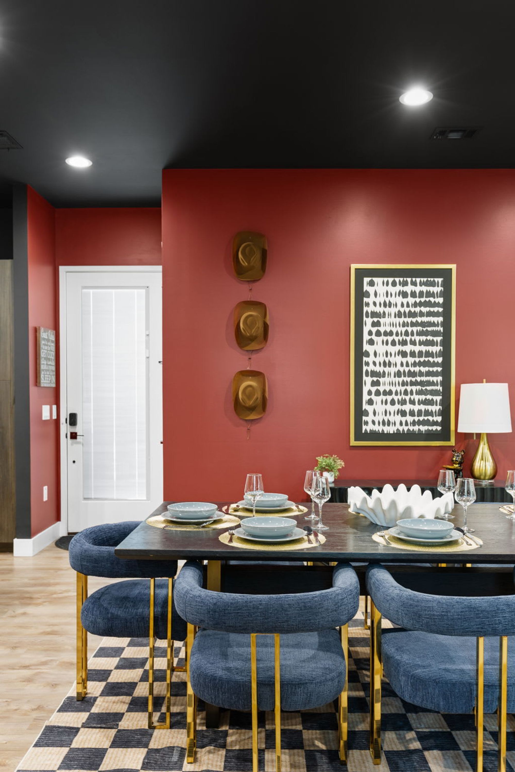 A dining area with a red wall, a framed abstract art piece, and a checkered floor.
