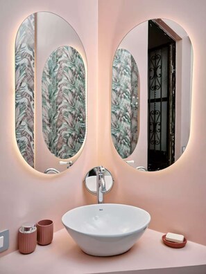 A bathroom with a white sink, two oval mirrors, and a floral wallpaper. - w Charming Apartment in Milan (Milan)