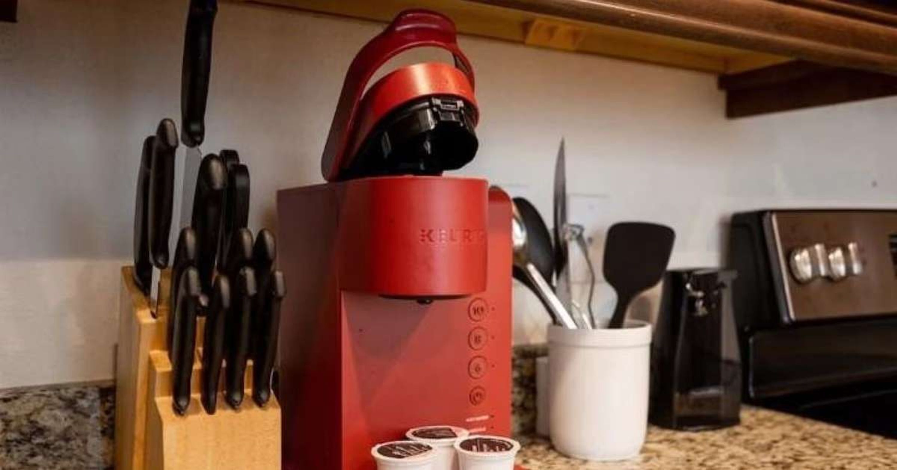 A red kitchen appliance with a handle, a knife block, and a white container with utensils.