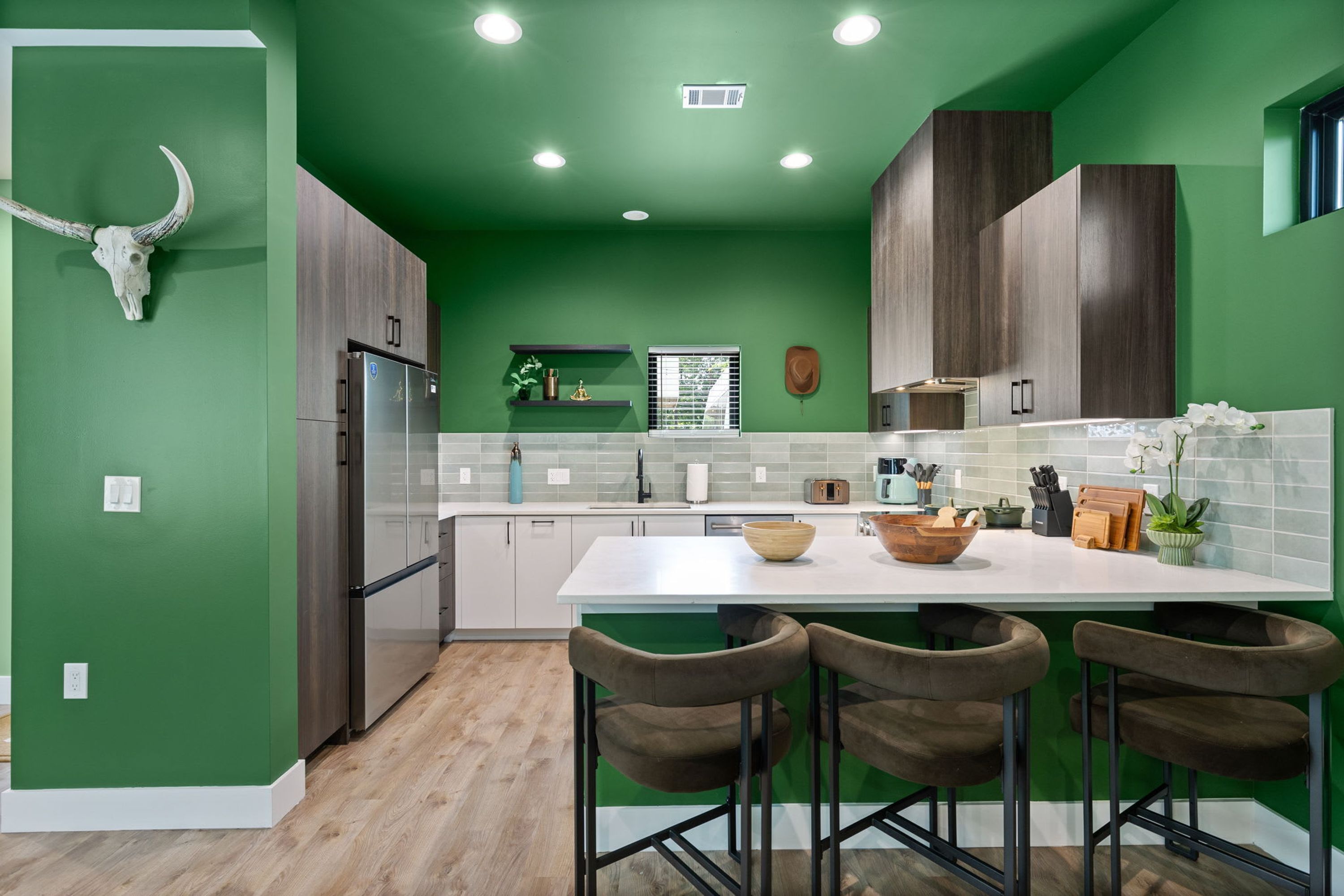 Una cocina moderna con paredes verdes, una isla blanca y taburetes de bar.