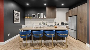 Uma cozinha moderna com uma ilha central, banquetas e uma geladeira.