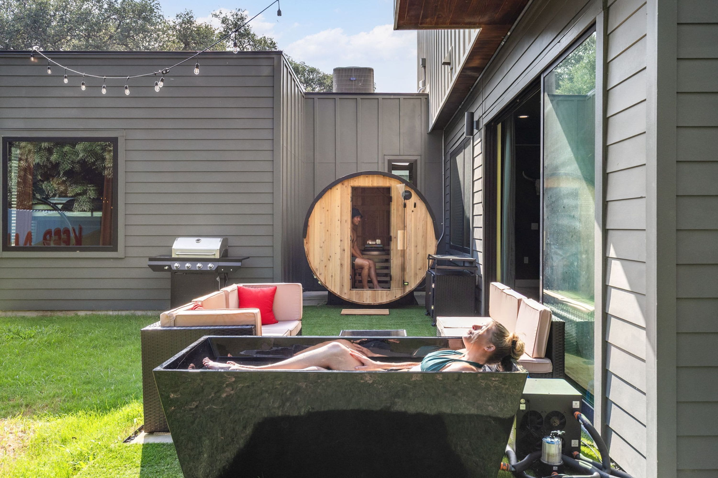 Un patio trasero con un jacuzzi, una sauna de madera y una parrilla de barbacoa.