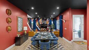 Uma sala de jantar com piso xadrez, uma mesa central posta para seis pessoas, e uma escada que leva a um andar superior.