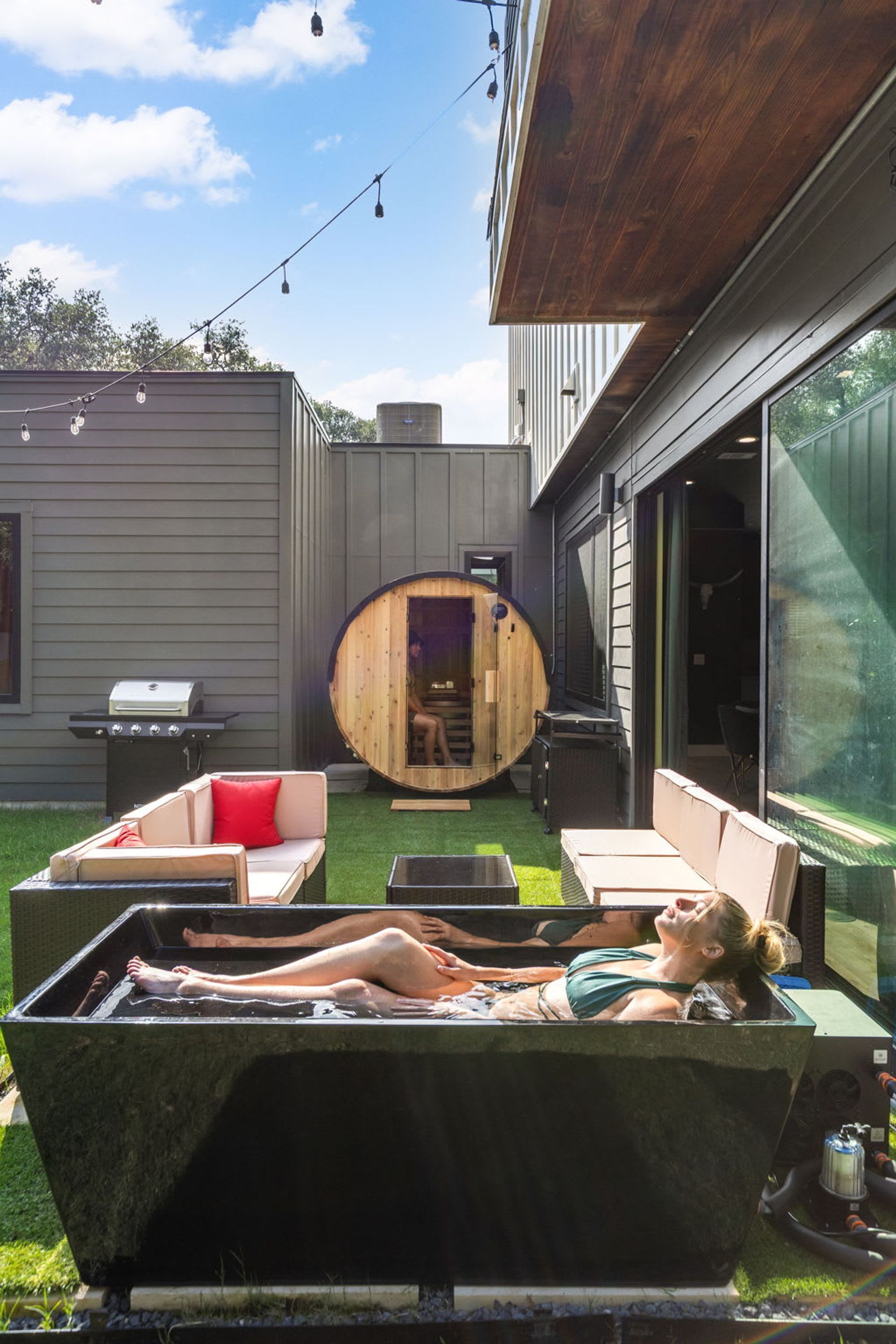 A modern outdoor relaxation area with a hot tub, lounge chairs, and a wooden sauna.