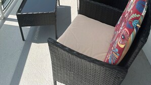 En balkong med möbler i rotting, ett glasbord och utsikt över havet.