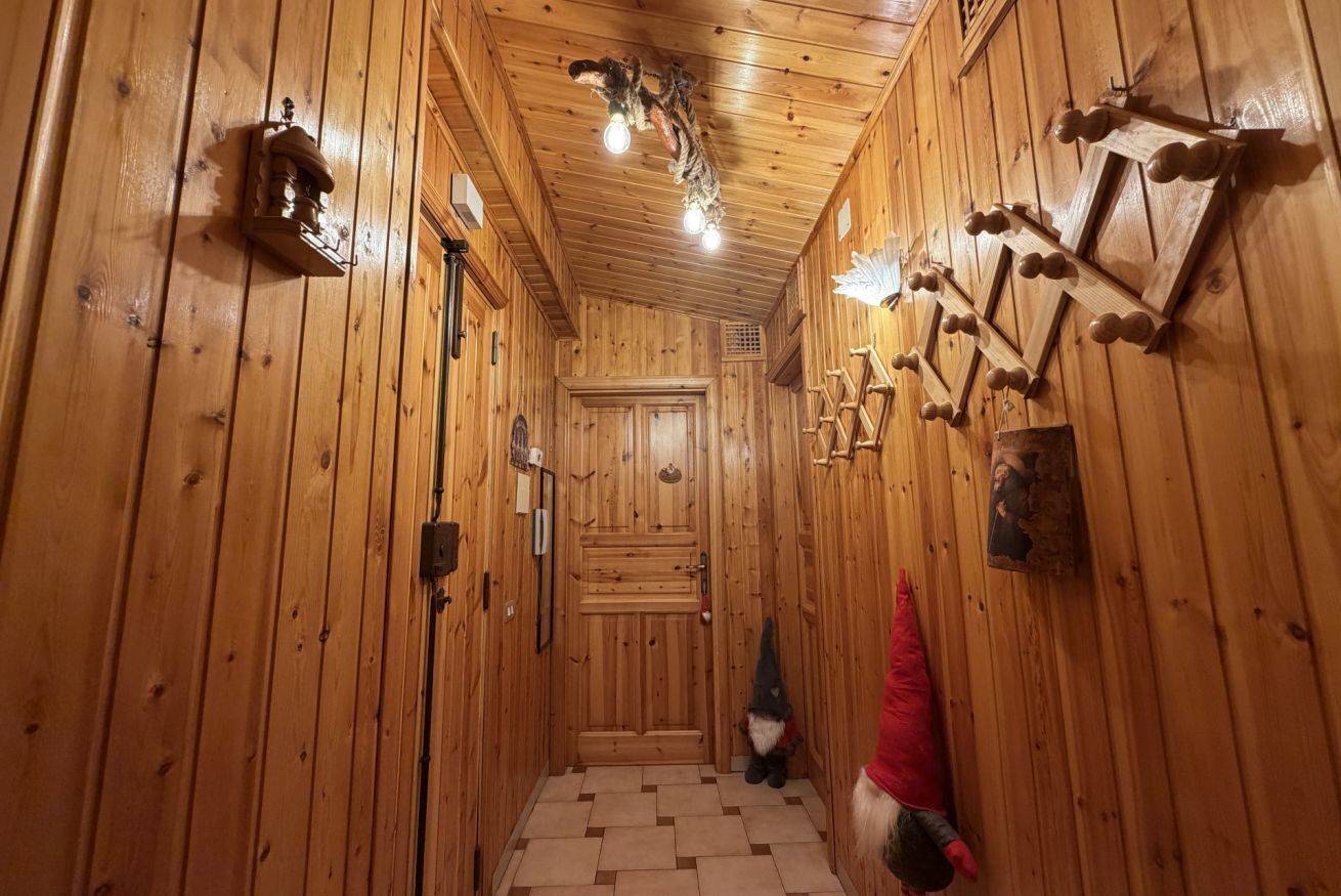 Um corredor de madeira com uma porta no final, uma decoração de gnomo e ganchos fixados na parede.