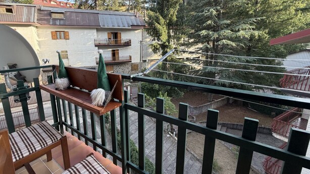 Un balcone con una panchina e sedie, che si affaccia su un cortile con alberi e un edificio.