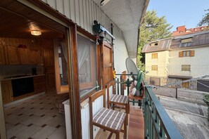 En balkon med gelænder af træ, en parabolsatellit og udsigt til nabobygninger.