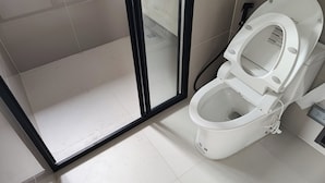 A bathroom with a white toilet, a glass shower enclosure, and tiled flooring. - Room-exclusive Holiday House in Thon Bur (Bangkok)