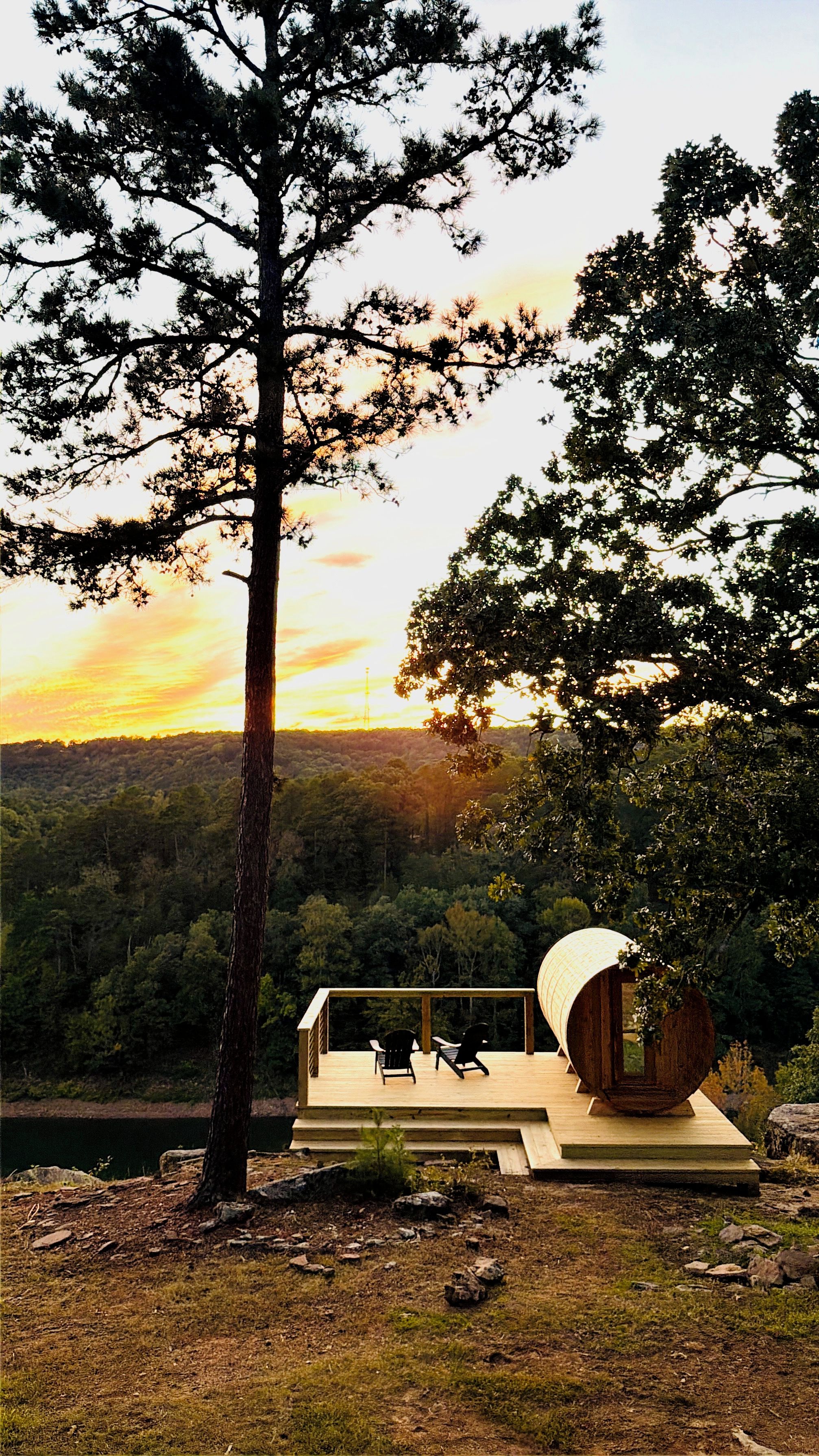 Terraza de madera con dos sillas, con vistas a un paisaje boscoso al atardecer.