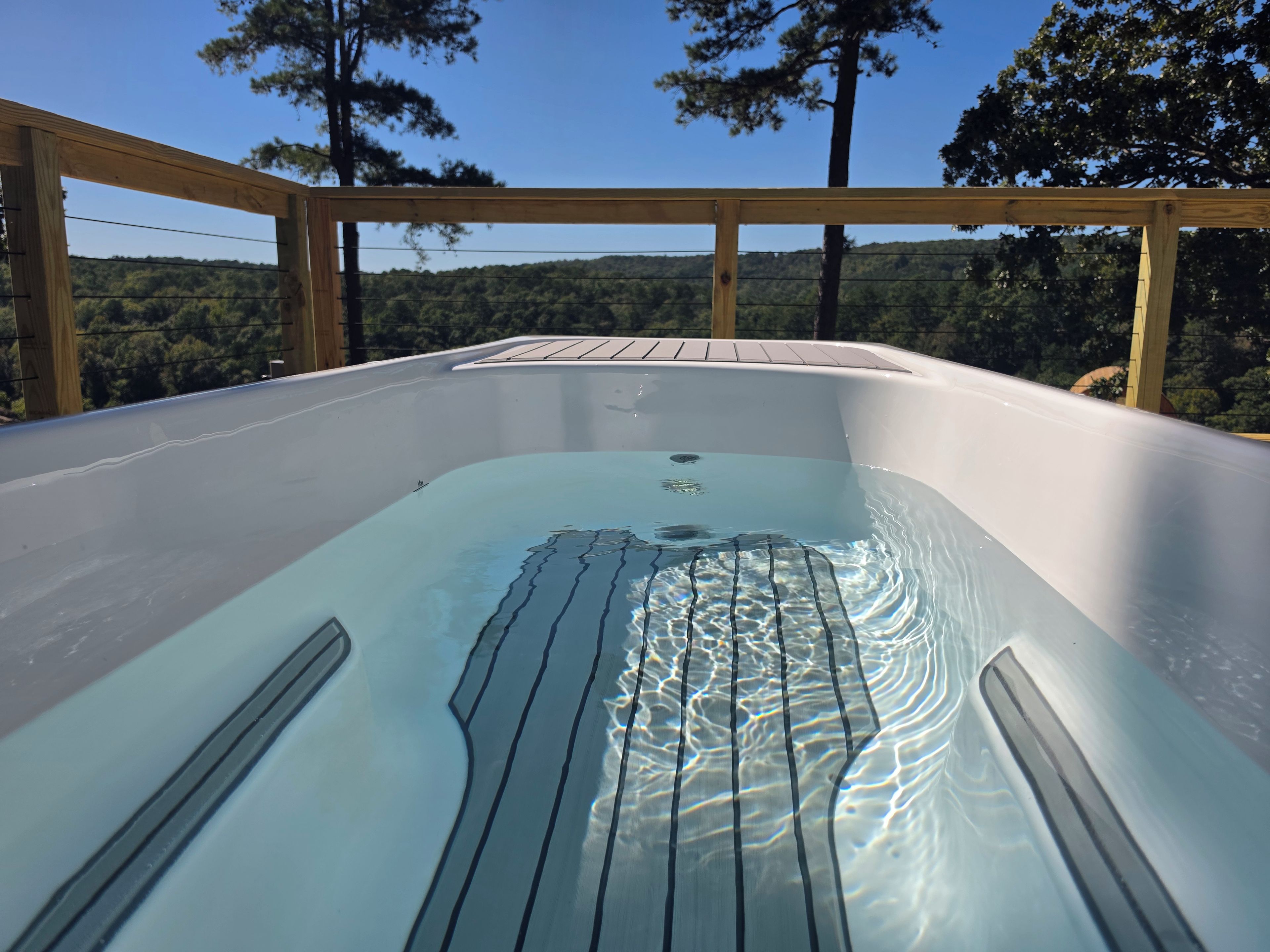 Un jacuzzi con cubierta de madera y vista a una ladera boscosa.