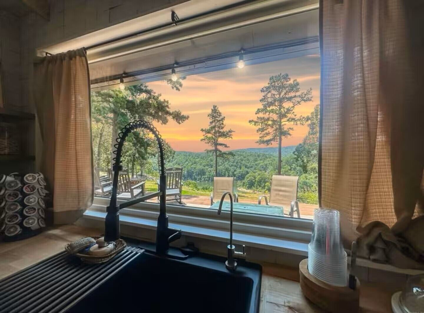 A room with a large window overlooking a forested landscape during sunset.
