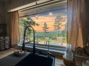 Una habitación con un ventanal grande que da a un paisaje boscoso al atardecer.