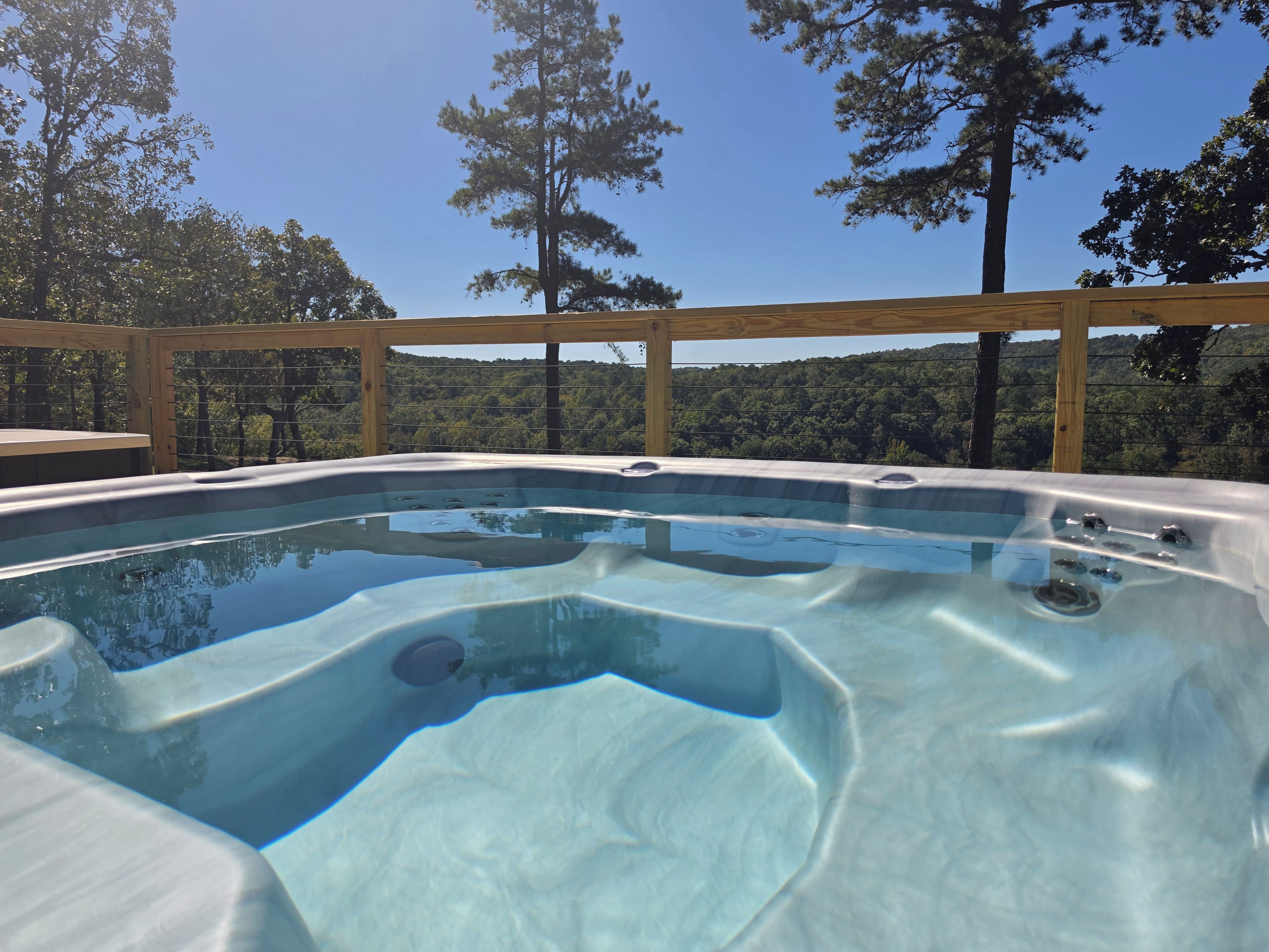 Ein Whirlpool mit Holzterrasse und Blick auf eine bewaldete Landschaft.