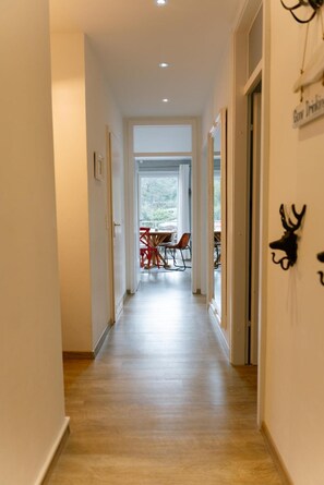 A hallway with a wooden floor leading to a dining area with a table and chairs.