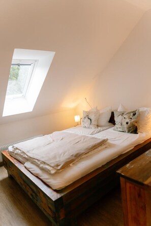 A bedroom with a sloped ceiling, a skylight, a bed with white bedding, and a bedside lamp.