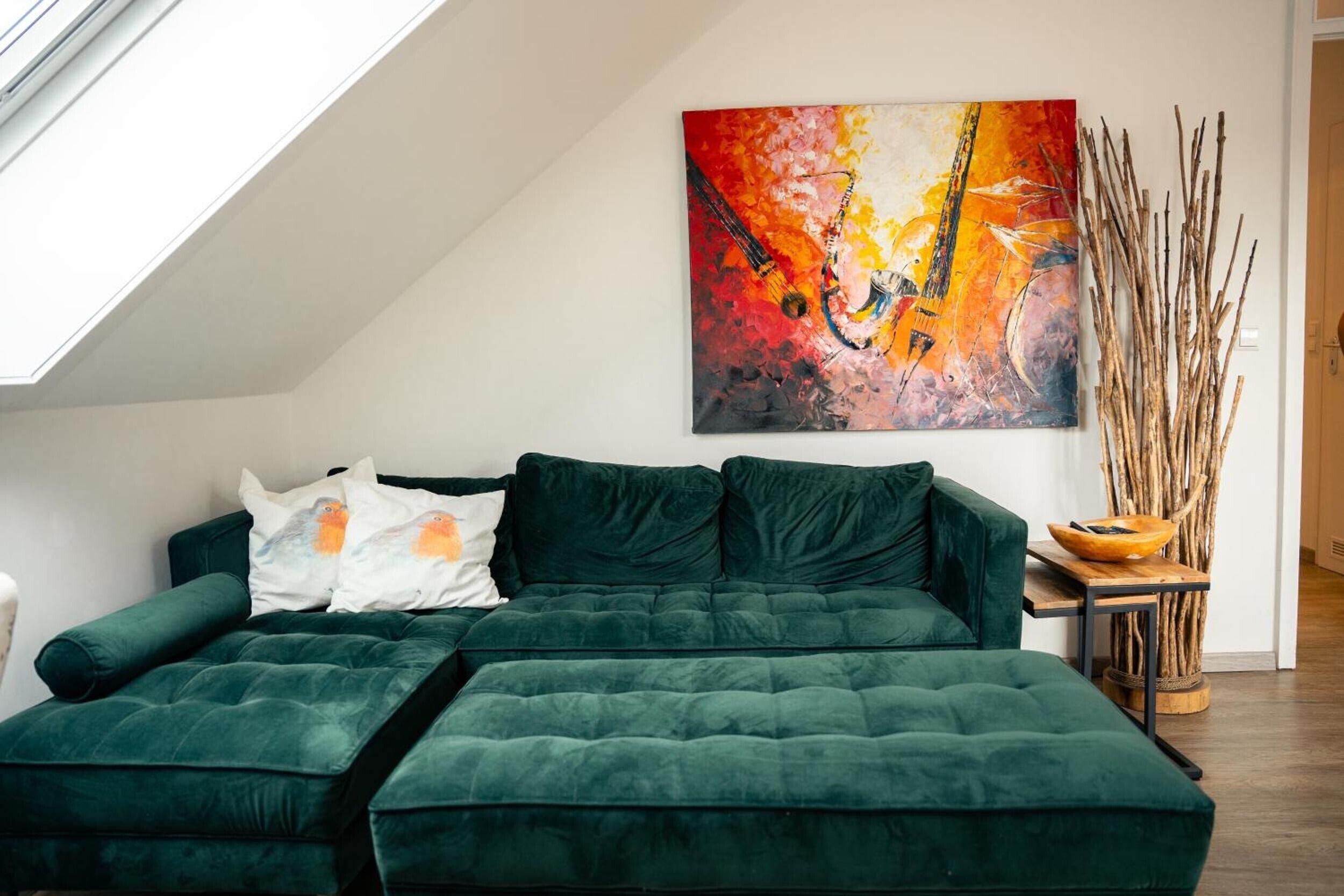 A green sectional sofa with pillows, a painting on the wall, and a wooden side table with a bowl.