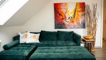 Ein grünes Ecksofa mit Kissen, ein Bild an der Wand und ein Holztischchen mit einer Schale.
