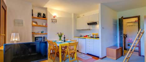 A compact living space with a dining area, kitchenette, and a television.