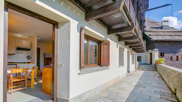 A corridor with a wooden bench and a table, leading to a room with a kitchen area. - Appartamento I Larici (Sauze di Cesana)